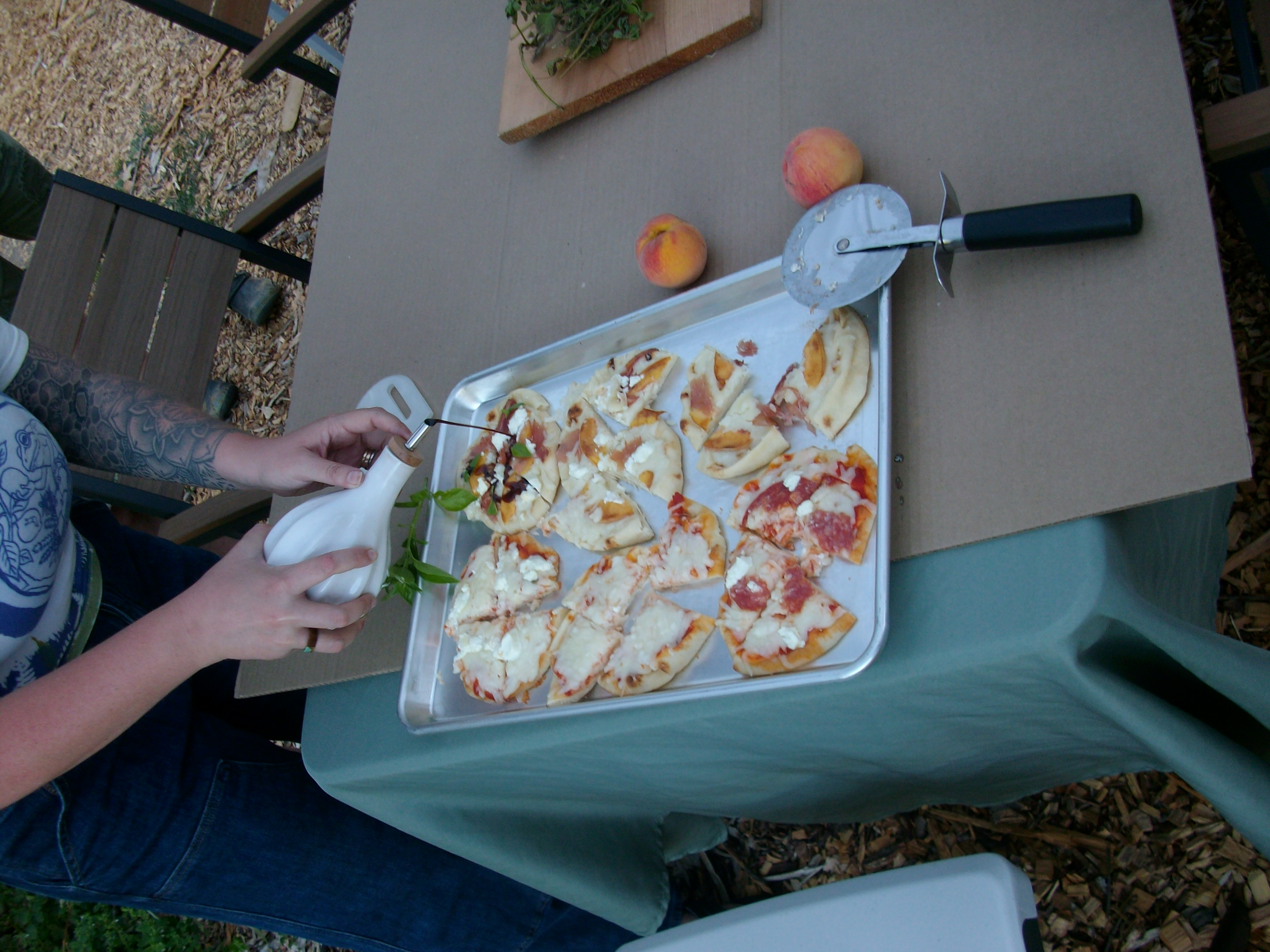 A picture of a tray of small pizzas, with hands coming in from off camera to drizzle a bottle of balsamic vinegar on one of the pizzas